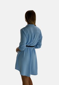 Light blue, long-sleeve shirt dress with a slim black belt at the waist, featuring a buttoned collar and gathered back detail.