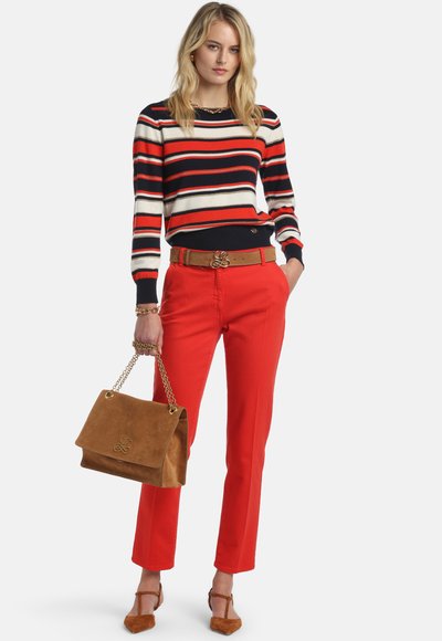 Pull rayé rouge, marine et crème, associé à un pantalon rouge vif. Porte un sac à main en daim marron avec une sangle en chaîne dorée.