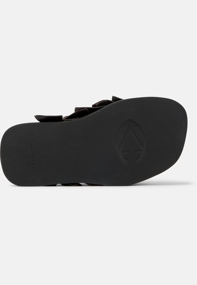 Černá podrážka sandálu s vyraženým logem a textem, zobrazuje texturovaný spodek a část horních pásků na bílém pozadí.