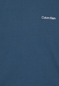 Tamsiai mėlyna medvilninė marškinėlių su apvaliu kaklu, ant viršutinio kairiojo krašto esantis mažas baltas "Calvin Klein" logotipas. Minkšta tekstūra.