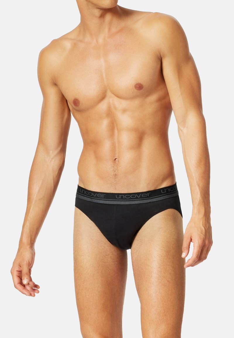 Schwarze Baumwollslips mit einem grauen elastischen Bund, auf dem der Markenname steht. Sie sind für eine enge Passform und eine glatte Textur ausgelegt.