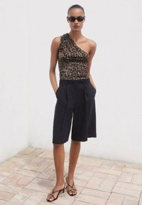 Top asimmetrico con stampa leopardata abbinato a pantaloni neri a vita alta e a pieghe. Indossato con sandali con cinghie e occhiali da sole scuri.