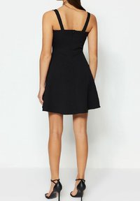 Robe noire sans manches avec un corsage ajusté et une jupe évasée. Dispose d'une fermeture éclair au dos et d'une texture de tissu lisse.