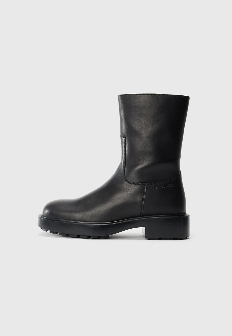 Botte en cuir noire mi-mollet avec bout rond, semelle plateforme épaisse et petit talon, vue de profil extérieur sur fond uni.