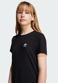 Melna ribota T-kreklā ar apaļu kakla izgriezumu un īsām piedurknēm. Uz krūšu ir neliels balts Adidas logotips. Mīksta auduma struktūra.