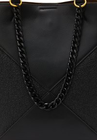 Sort tote taske med teksturerede og glatte lædersektioner, en sort kædetræk og guldhardware detaljer. Vinklet design med en ren finish.