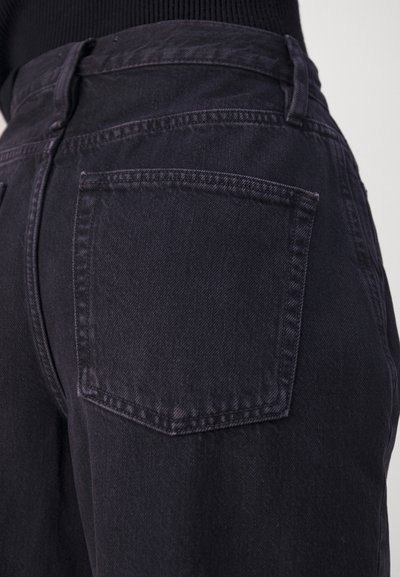 Un jean en denim noir taille haute avec un design à cinq poches, comprenant une poche arrière visible et une texture subtile. Coutures détaillées le long des seams.