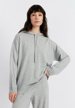 Sweatshirt à capuche grise en tissu doux et tricoté. Présente un col zippé mi-haut, des manches larges et un ourlet côtelé. Associé à un bas assorti.