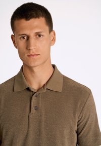 Brun polo-tröja i texturerat tyg, med krage, korta ärmar och tre knappar på fronten.