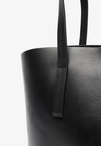 Sac en cuir noir de forme tote, avec une texture lisse, une forme cylindrique et des poignées plates présentant des détails de couture précis.