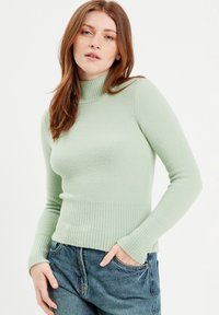 Hellgrüner, gerippter Rollkragenpullover mit strukturierter Oberfläche. Figurbetonter Stil mit langen Ärmeln, kombiniert mit blauen Jeans.