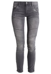 Šedé denimové džíny s odřenými nášivkami, žebrovaným detailem na kolenou a zipovými lemy. Úzký střih, pět kapsových styl a poutka na pás.