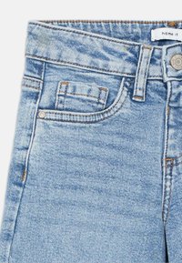 Jean en denim bleu clair à taille haute, avec un design à cinq poches et des coutures contrastées. Comprend un bouton en métal et une fermeture éclair.