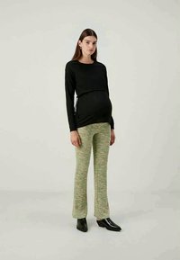 Svart langermet topp med lagdelt design, kombinert med grønne strukturerte vide bukser og svarte spisse sko.