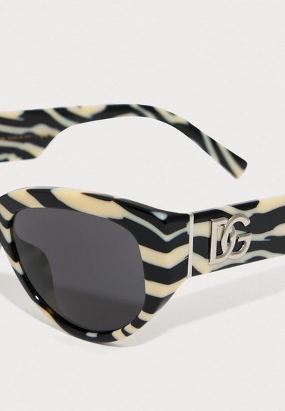 Schwarz- und elfenbeinfarbene, gemusterte Sonnenbrille mit dickem Rahmen, ausgestattet mit einem dunkel verlaufenden Glas und einem metallischen Logo-Akzent am Bügel.