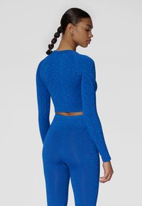 Niebieski zestaw sportowy składający się z dopasowanej topu z długim rękawem oraz legginsów z wysokim stanem, oba z subtelnym zwierzęcym wzorem i bezszwowym wykonaniem.