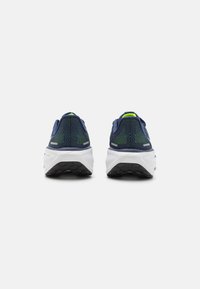 Baskets de sport navy avec une tige en mesh texturé, semelle intermédiaire blanche et semelle en caoutchouc noir ; présente des accents bleus et verts au niveau du talon.