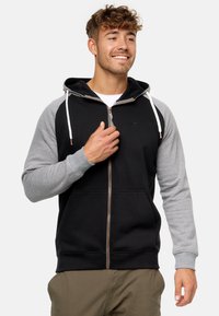 Sudadera con capucha y cremallera, con un cuerpo negro y mangas grises, confeccionada en tela suave con un bolsillo tipo canguro y detalles de cordón.