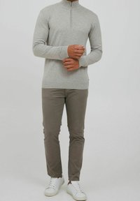 Grijze trui met ritssluiting, geribbelde mouwen en zoom, gecombineerd met lichtgrijze broek en witte sneakers. Soepele textuur, slim-fit ontwerp.