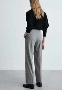 Pantalons gris ajustés en tissu structuré, présentant une coupe droite, des poches latérales et un design lisse à l'arrière.