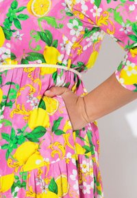Abito rosa con un motivo di limoni e fiori, maniche corte, vita cinchata e una tasca laterale. Tessuto morbido e leggero.