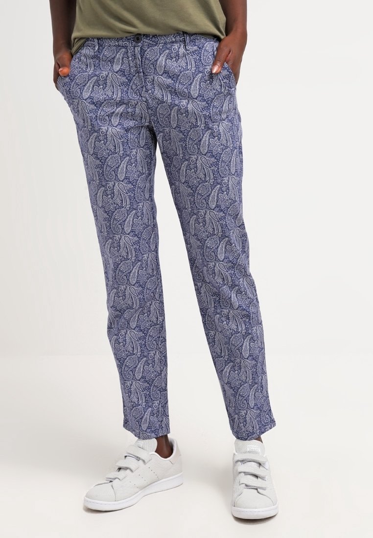 Pantalons à motif paisley bleu en tissu léger, avec une coupe décontractée, des poches latérales et des chevilles retroussées, associés à des baskets blanches.