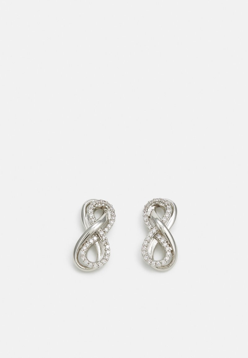 Boucles d’oreilles en argent en forme d’infini avec une bande lisse torsadée et une bande incrustée de petits cristaux transparents sur fond blanc.