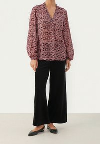 Rosa Bluse mit floralem Muster, langen Ärmeln und V-Ausschnitt. Kombiniert mit schwarzen weit geschnittenen Kordhosen und schwarzen Ballerinas.