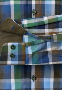 Langarmige blouse met een groen, blauw, bruin en wit ruitpatroon, toont een opgerolde manchette met donkergroene knopen.