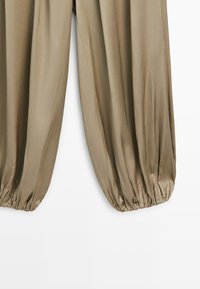 Pantalon en tissu beige avec des poignets élastiques froncés, créant une silhouette de jambe fuselée en forme de ballon.