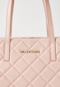 Rožinė guminė odinė rankinė su auksiniu "VALENTINO" logotipu ir dviem tvirtomis rankenomis. Pasižymi deimantų raštu ir lygiu paviršiumi.