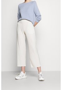 Světle modrý pletený svetr s ohrnutými rukávy, v kombinaci s bílými kalhotami se širokými nohavicemi a šedobílými sportovními teniskami. Hladká textura a uvolněný střih.