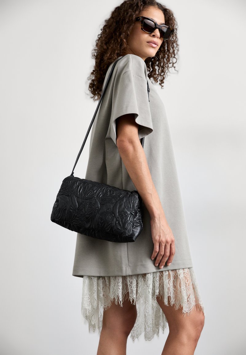 Γκρίζο υπερμέγεθες φόρεμα μπλούζα με δαντελένιο τελείωμα, συνδυασμένο με μια μαύρη δερμάτινη τσάντα εξώφυλλου. Τα γυαλιά ηλίου ολοκληρώνουν το σύνολο.