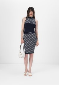 Robe en maille deux pièces de couleur marine, composée d'un haut sans manches et d'une jupe à motifs. Les accessoires incluent un sac à main blanc et des sandales claires.
