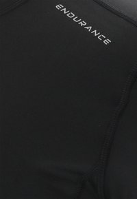 Zwarte sportshirt gemaakt van rekbare stof, met een ronde halslijn en platte stiksels. Het "ENDURANCE" logo in zilver is zichtbaar aan de bovenkant links.