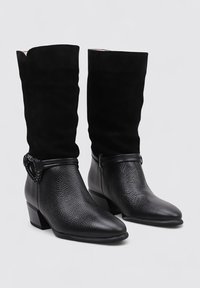 Botas de cuero negro hasta el tobillo con acabado texturizado, punta afilada y tacón bajo tipo bloque. Presentan un caño de ante negro y detalle de correa decorativa.