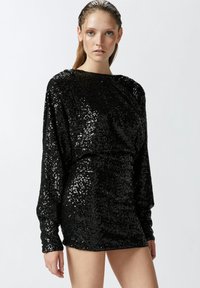 Crna haljina s kamenčićima, dugih rukava, uskog siluete i blago napuhanih ramena. Glatka tekstura s sjajnim završetkom.