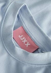 T-shirt azzurro chiaro con scollatura tonda, dotato di un'etichetta del marchio rosa visibile all'interno del colletto. Tessuto liscio con una texture sottile.