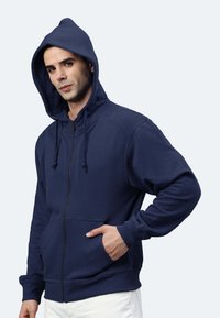 Felpa con zip di colore blu navy, dotata di cappuccio regolabile con lacci, tasca a marsupio, polsini a costine e una texture liscia.