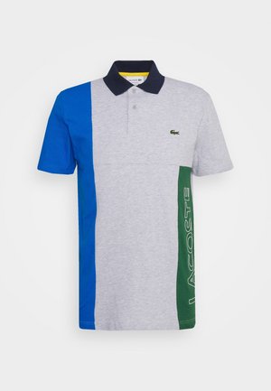 Polo à manches courtes avec devant gris, panneau gauche bleu, panneau droit vert avec texte "Lacoste" et col noir avec deux boutons.