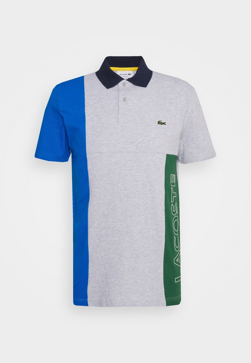 Polo à manches courtes avec devant gris, panneau gauche bleu, panneau droit vert avec texte "Lacoste" et col noir avec deux boutons.