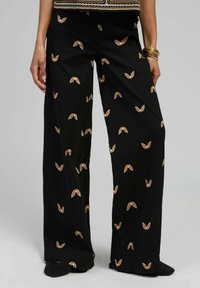 Pantalons noirs à jambe large avec une texture douce, présentant un motif géométrique répétitif de petites formes brunes et blanches.