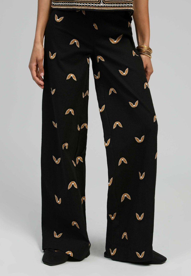 Pantalons noirs à jambe large avec une texture douce, présentant un motif géométrique répétitif de petites formes brunes et blanches.