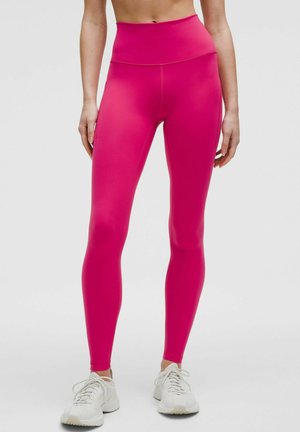 Leggings a vita alta di un rosa brillante, realizzati in materiale elasticizzato. Presentano una texture liscia e un design aderente, abbinati a sneakers leggere.