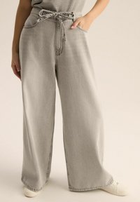 Jasnoszare dżinsy o szerokich nogawkach z elastycznym pasem, kieszeniami bocznymi, widocznymi szwami i luźnym krojem. Subtelna tekstura o gładkim wykończeniu.