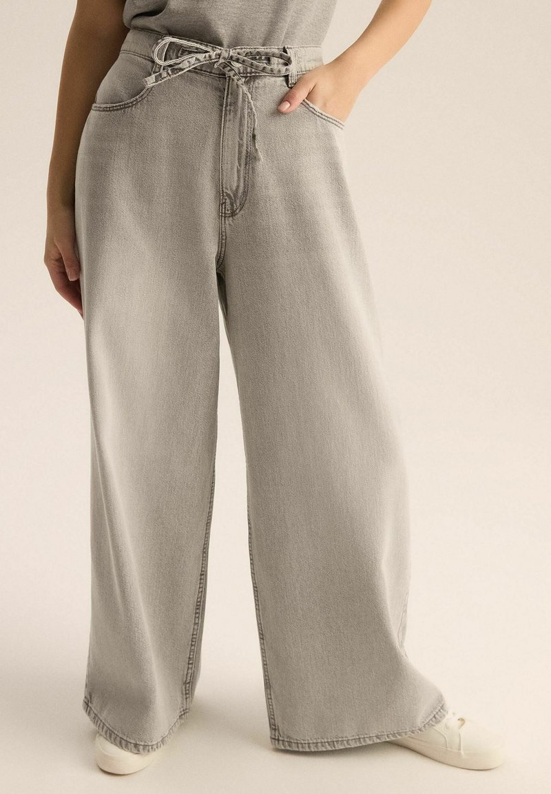 Jasnoszare dżinsy o szerokich nogawkach z elastycznym pasem, kieszeniami bocznymi, widocznymi szwami i luźnym krojem. Subtelna tekstura o gładkim wykończeniu.
