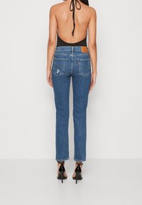 Högtaljade blå denimjeans med raka ben, med bakfickor och en läderlogotyp. Kombinerat med en svart halterbodysuit.