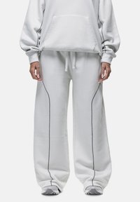 Hellgraues, übergroßes Hoodie mit Vordertasche, kombiniert mit lockeren Hosen, die dunkelgraue Seitennaht und elastischen Bund haben. Glatte Textur.