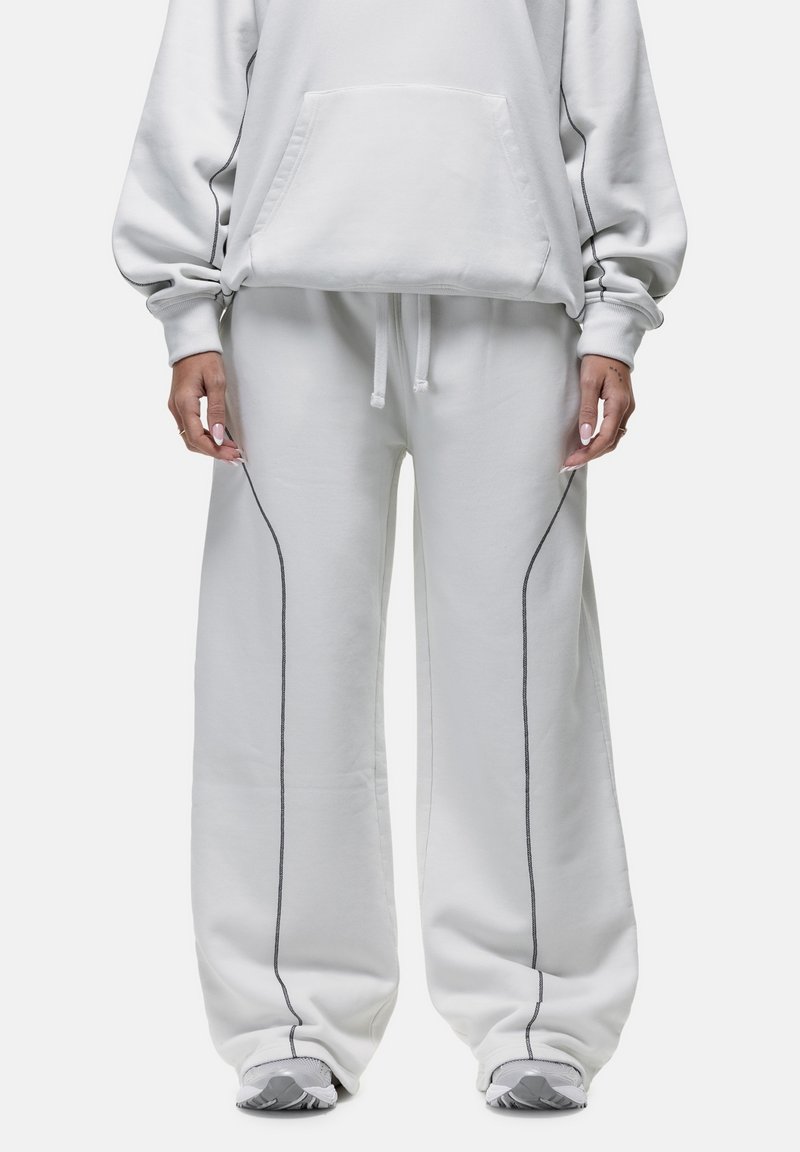 Hellgraues, übergroßes Hoodie mit Vordertasche, kombiniert mit lockeren Hosen, die dunkelgraue Seitennaht und elastischen Bund haben. Glatte Textur.