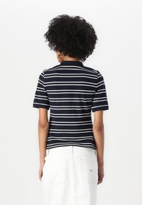Poloko s krátkým rukávem a límcem v námořnické modré a bílé pruhované barvě. Hladká textura a slim fit, v kombinaci s bílými džíny s vysokým pasem.